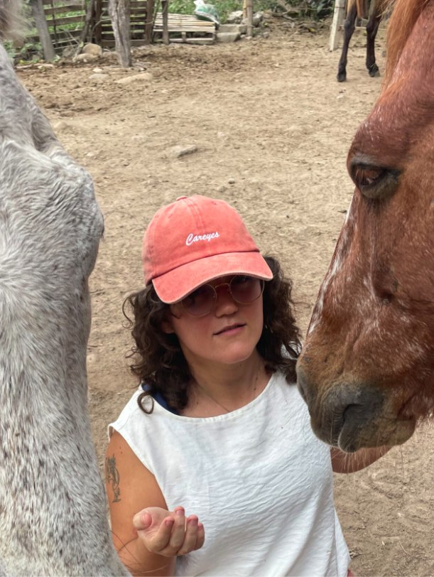 Una mujer ofrece la mano abierta entre las cabezas de dos caballos