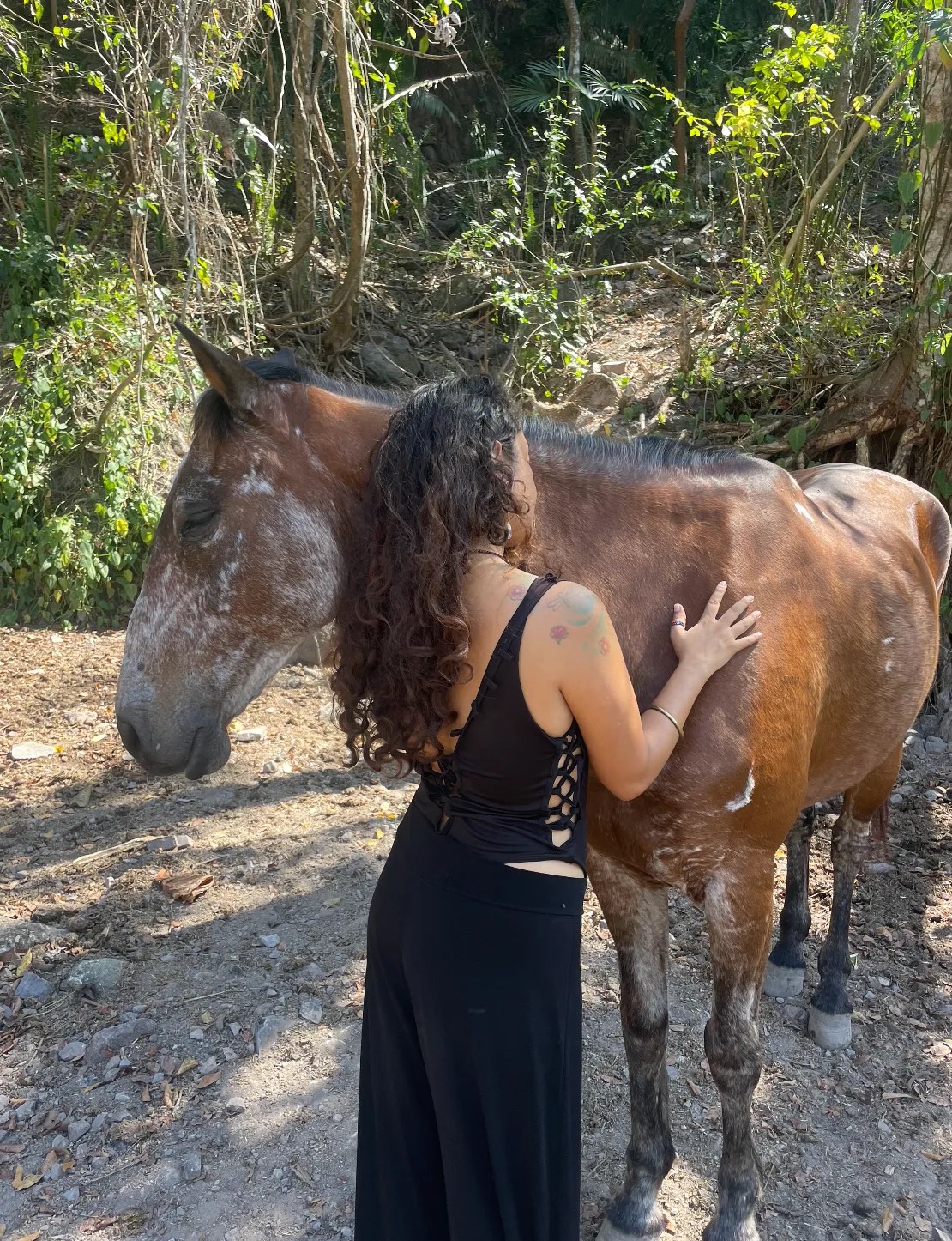 Erika apoyada en el cuello de un caballo castaño, de espaldas, en el bosque