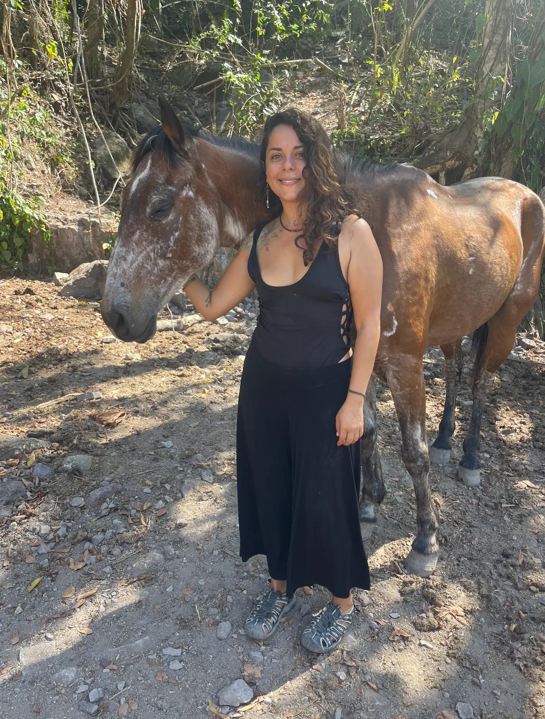Erika de pie junto a un caballo tordo, con la mano apoyada en su cuello
