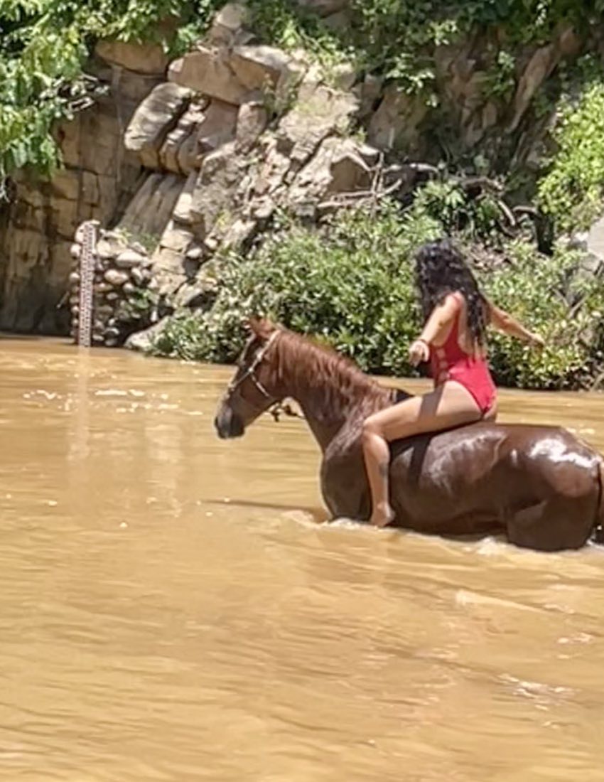 Una mujer recostada sobre el lomo de un caballo dentro del agua