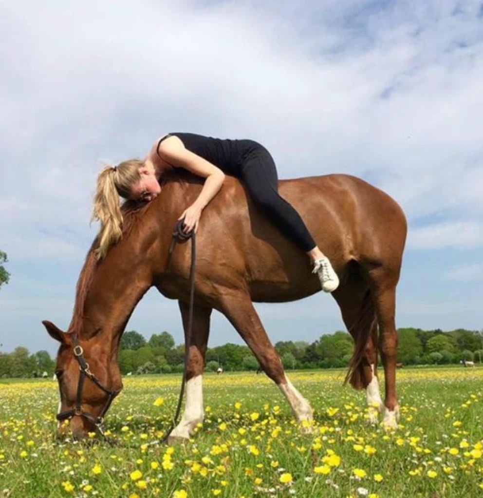 Una mujer recostada sobre el lomo de un caballo que pasta en un prado florido