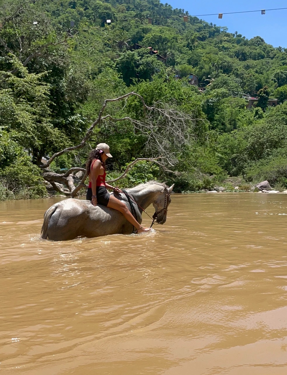 Una mujer sentada sobre un caballo tordo dentro del río, en Puerto Vallarta